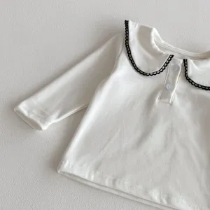 Close-up of baby white long-sleeve top featuring a black scalloped collar and buttons.