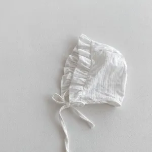 Gros plan sur un délicat bonnet de bébé blanc avec de charmants volants et des liens noués.