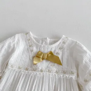 Gros plan sur une barboteuse pour bébé fille blanche avec dentelle délicate et nœud doré.