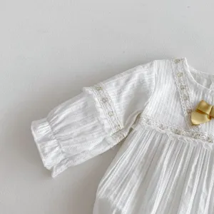 Vue détaillée d'un barboteuse bébé fille blanche en dentelle à manches longues et nœud d'or.