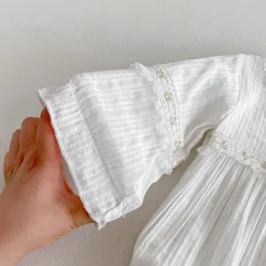 Vue détaillée de la manche de barboteuse blanche pour bébé avec bordure en dentelle délicate.