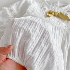 Détail du tissu du sarouel bébé fille blanc avec nœud mignon et bordure en dentelle.