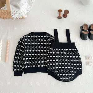 Close-up detail of infant baby knit cardigan and suspender romper set with black white pattern.