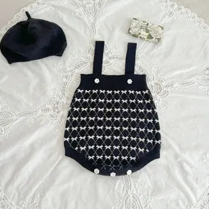Close-up detail shot of the elegant black knit baby romper featuring white flower buttons.