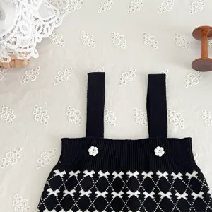 Cute black knit baby strap romper featuring white floral buttons and chic geometric pattern.