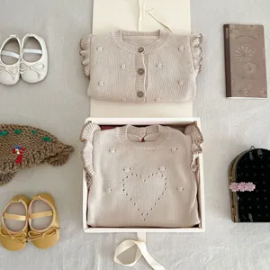 Detailansicht des Babystrick-Sets mit süßer Rüschenjacke und Herz-Pullover im Flatlay.