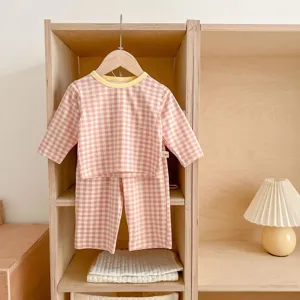 Detailed view of pink gingham baby pajama set hanging on wooden shelf with warm lighting.