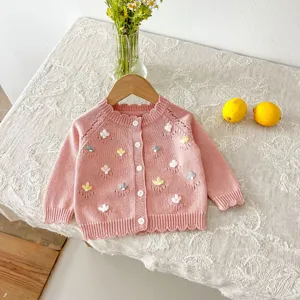 Close-up detail of pink baby girl knitted cardigan with delicate handmade floral embroidery.