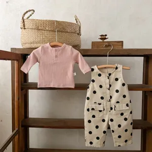Detailansicht des Babymode Sets mit rosa Rippshirt und gepunktetem Strampler an Holzbügeln.