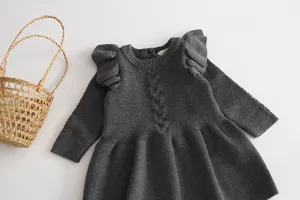 Detailed view of baby girl's dark grey knitted dress featuring cute ruffled shoulders and cable knit design.