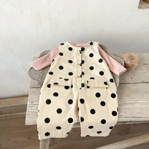 Detailansicht von Baby Mädchen Pünktchen Latzhose und rosa Oberteil auf rustikalem Holzhintergrund.
