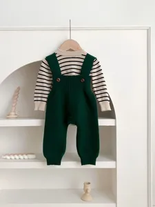 Detailed view of baby knit striped top and green overalls set hanging on a clean white shelf.