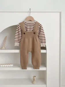 Baby knit sweater and overalls set detail, cute striped top on white arch shelf background.