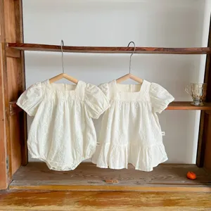 Close-up details of white embroidered baby toddler romper and dress set on wooden hangers.