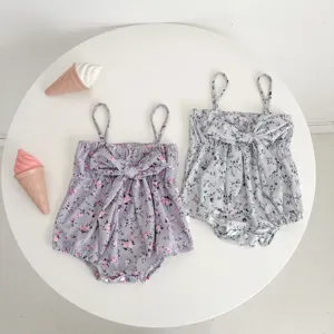 Detailed close-up view of infant floral camisole romper with cute front bow on a white table.