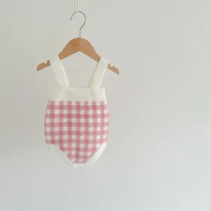 Détail de barboteuse bébé en tricot à carreaux rose et blanc, bretelles et boutons.