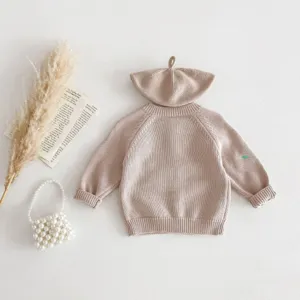 Detail shot of baby knitted cardigan sweater with matching hat, beige color and cute embroidery.