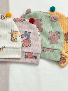 Close-up detail of newborn waffle baby beanies with cute animal prints and soft pom-pom accents.