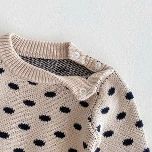 Baby infant knitted sweater detail shot, beige cotton fabric with navy dots, shoulder snaps.
