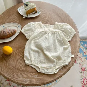 Detailed shot of baby summer embroidered puff sleeve romper on wooden table with cute props.