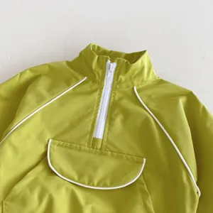 Detalle de chaqueta cortavientos verde para niños, cuello alto con cremallera blanca y vivo.