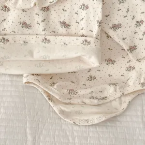Infant floral cotton romper detail shot, showcasing soft fabric, ruffle collar and snap buttons.