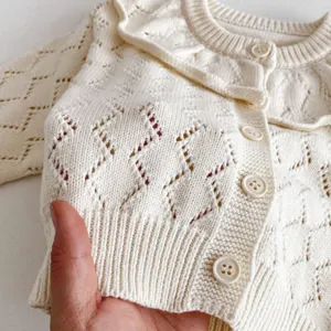 Close-up of baby girl knitted cardigan featuring hollow diamond pattern and ruffles.