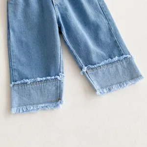 Close-up detail of girls light blue denim jeans showing cuffed frayed hem design, soft fabric.