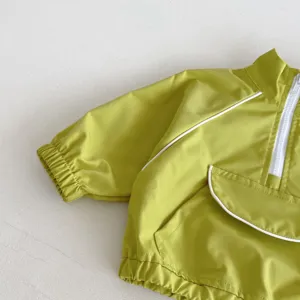 Detalle de chaqueta infantil, tela verde clara con ribete blanco y bolsillo con cremallera.