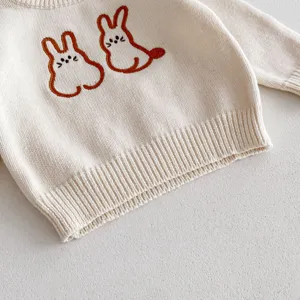 Cute baby sweater knit detail showing embroidered brown cartoon bunnies on soft beige cotton fabric.