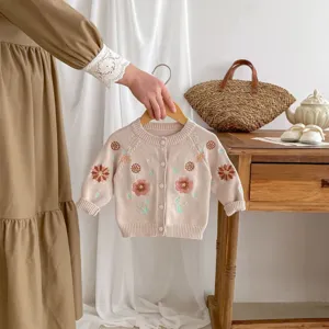 Close-up detail of infant knitted cardigan with floral embroidery and wooden buttons.