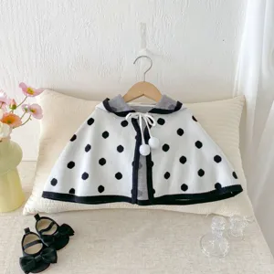 Dettaglio mantella in maglia a pois neri e bianchi per neonati, capo accogliente con pon pon.