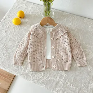 Detailed shot of baby knit cardigan with ruffle collar and wooden hanger on floral background.