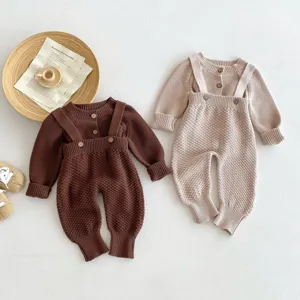 Dettaglio di un grazioso set in maglia per neonati con cardigan e pantaloni con bretelle.