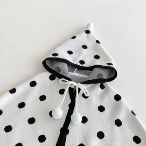 Primo piano di mantella lavorata a maglia per neonati con pois neri e pompon decorativi.