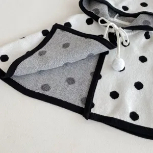 Dettaglio mantella con cappuccio in maglia per neonati, motivo pois neri, morbida.