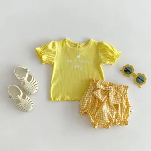Dettaglio di t-shirt estiva per bambini in cotone a coste giallo e pantaloncini a quadri