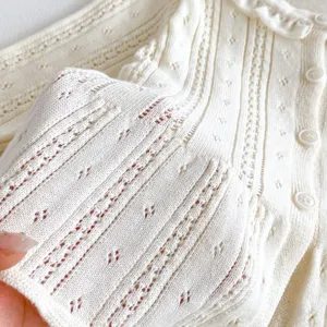 Close-up detail of infant knit cardigan showing breathable hollow-out cotton texture and buttons.
