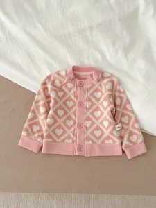 Vue détaillée du gilet en tricot rose pour bébé avec motif de cœur et boutons.