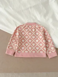 Mignon gilet pull en tricot rose pour bébé avec joli motif de losanges et de cœurs.