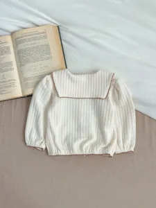 Primeros planos de los detalles del cárdigan de punto para bebé, top blanco con cuello marinero.