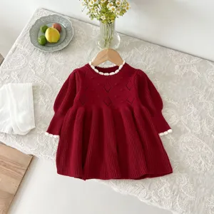 Detailed view of a cute red baby girl knitted dress with white lace trim and long sleeves.
