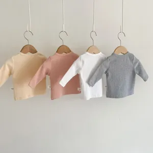 Details of soft ribbed cotton baby long sleeve shirts in four colors, hanging on wooden hangers.