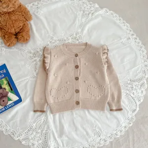 Detailaufnahme der Babystrickjacke mit Rüschenschultern und Herzstrickmuster, gemütlich.