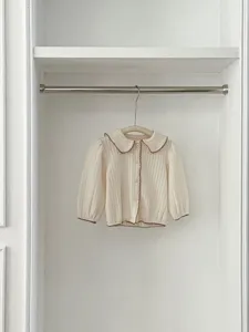 Vista detallada del cárdigan blanco para bebé con cuello de muñeca y puños marrones.