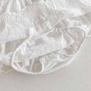 Close-up detail of infant baby girl white cotton lace romper with delicate embroidery.