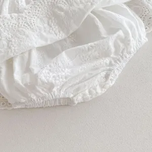 Close-up detail of white baby girl cotton lace romper, delicate embroidery and elastic edges.