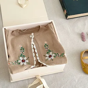 Infant baby knitted cardigan with floral embroidery and white trim in detail view.