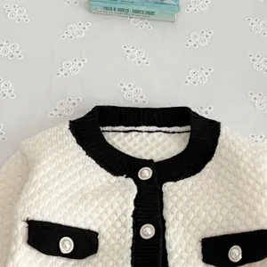 Nahaufnahme Detailansicht des Baby Strickcardigans mit schwarzem Kontrast und Perlenknöpfen.