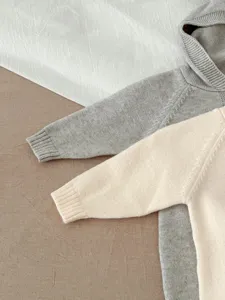 Vista detallada de mameluco tejido con capucha para bebé gris y beige, tela suave infantil.